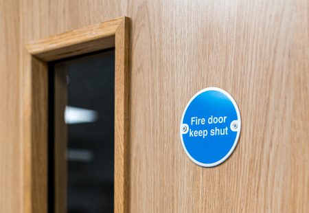 Close-up of a typical Fire Door Keep Shut sign seen on an interior door within a British hospital. The firedog prevents any fire or smoke spreading in the building.